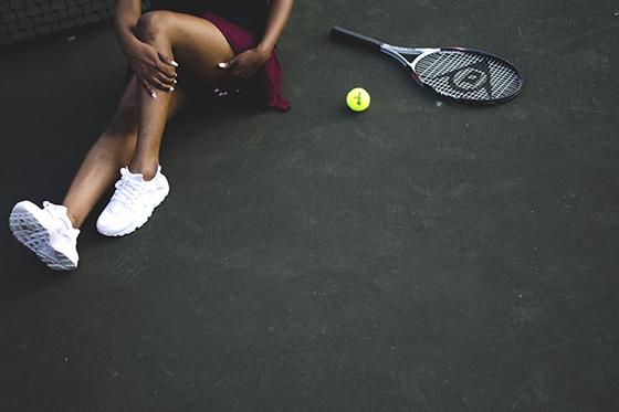 Photo from above of a woman adjusting her leg, sitting next to a tennis racket and ball. 